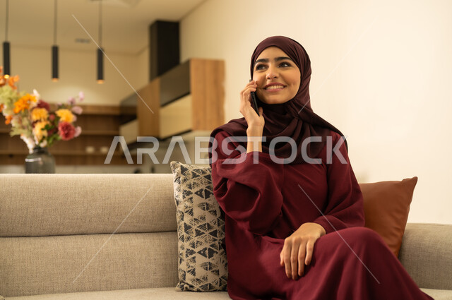ايماءات السعادة والسرور، صورة مقربة لإمراة عربية خليجية سعويدة ترتدى العباءة والحجاب ، تقوم باجراء مكالمة هاتفية عبر الهاتف المحمول، دمج التقنيات الحديثة بالحياة اليومية، امرأة عربية خليجية عمانية تقوم بالتواصل مع الاهل والاصدقاء عبر الجوال .