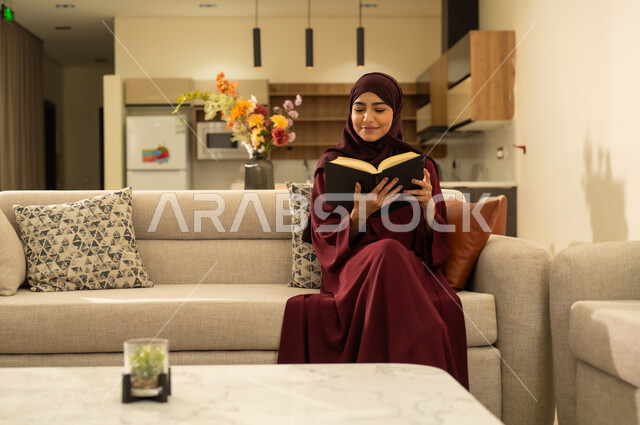 الشغف بممارسة الهوايات المفيدة ، إيماءات التركيز والاندماج, تمضية وقت الفراغ بالتعلم والتثقيف الذاتي ، إمراة عربية خليجية سعودية ترتدي العباءة والحجاب ، تجلس على اريكة مريحة وتحمل بيدها كتاب تثقيفي ، امرأة عربية خليجية عمانية تقوم بقراءة الكتب بتمعن ، الاستمتاع بقراءة الروايات والقصص .