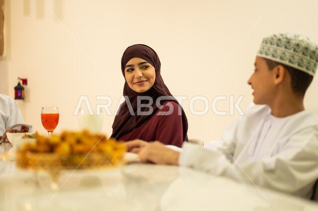 Building close relationships with family, gestures of happiness at the arrival of the holy month, exchanging conversations between mother and son, an Arab Gulf Omani family sitting at the iftar table during the month of Ramadan, Ramadan decorations and ornaments, delicious food and appetizers, the month of goodness and blessing.s