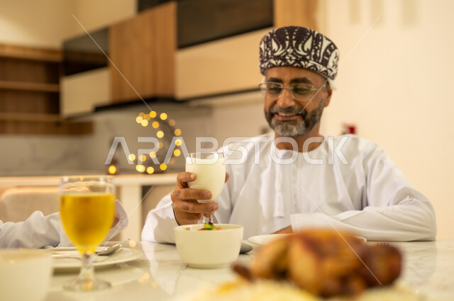 الاستمتاع بشرب العصائر المفيدة اللذيذة ، رجل عربي خليجي عماني يرتدى الدشداشة والكمة ويجتمع مع عائلته على مائدة الافطار فى شهر رمضان ، ايماءات الفرح والسعادة بقدوم الشهر المبارك ، ديكورات وزينة  شهر الخير والبركة .