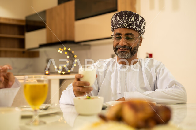 اجواء شهر رمضان المبارك ، رجل عربي خليجي عماني يرتدى الدشداشة والكمة ويستمتع بشرب العصير المفيد اللذيذ ،  اجتماع الأهل ومشاركة الطعام على مائده الإفطار ، ايماءات الفرح والسعادة بقدوم الشهر المبارك ، ديكورات وزينة  شهر الخير والبركة .