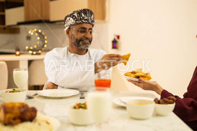 ايماءات الفرح والسعادة بقدوم شهر رمضان الفضيل , منتجات محلية عربية ، صورة مقربة ليد إمراه عربية خليجية عمانية تقدم طبق من السمبوسك المقرمشة لزوجها على مائدة الافطار فى شهر رمضان, المقبلات والمأكولات الشهية، ديكورات وزينة رمضانية ، شهر الخير والبركة .