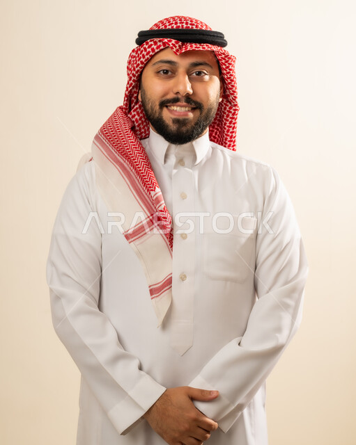 الاهتمام بالأناقة والمظهر الخارجي، بورتريه لرجل عربي خليجي سعودي مبتسم يرتدي الشماغ والثوب التقليدي ينظر إلى الكاميرا بإيماءات السرور، الشعور بالثقة في النفس، صورة شخصية للوثائق الرسمية، خلفية بيج.