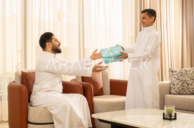 حب واحترام الآباء , إدخال السعادة والسرور إلى قلب الأهل, ولد عربي خليجي سعودي يرتدي الثوب التقليدي , يقدم هدية لوالده في أجواء العيد , إيماءات الفرح و البهجة, تقديم الهدايا فى المناسبات و العيد السعيد .
