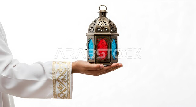 الاستعداد والتجهز لاستقبال شهر رمضان المبارك، الاحتفال بقدوم شهر الخير، بورتريه مقرب ليد امرأة عربية خليجية سعودية ترتدي عباءة بيضاء تحمل فانوس معدني مزخرف مضيء، زينة وأنوار الأعياد والمناسبات الدينية الاسلامية، خلفية بيضاء