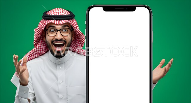 الإعلانات والعروض التسويقية عبر التقنيات والتكنولوجيا الحديثة، موك أب أبيض كبير، النظر إلى الكاميرا بايماءات الاستغراب والصدمة، بورتريه مقرب لرجل عربي خليجي سعودي يرتدي الثوب التقليدي والشماغ يقف امام مجسم ضخم لهاتف محمول بشاشة بيضاء فارغة، خلفية خضراء