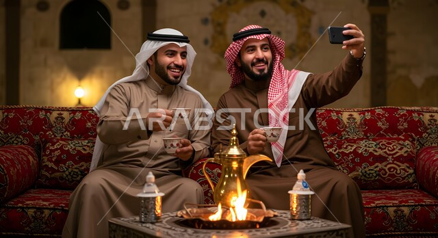  توثيق اللحظات السعيدة، مفهوم حسن الضيافه والاستقبال، رجل عربي خليجي سعودي يقوم بالتقاط صور السيلفي التذكارية مع صديقه باستخدام الهاتف الجوال، صديقان عربيان خليجيان سعوديان في جلسة بر وتخييم خارجية في الأجواء الشتوية، كشتة شعبية شبابية