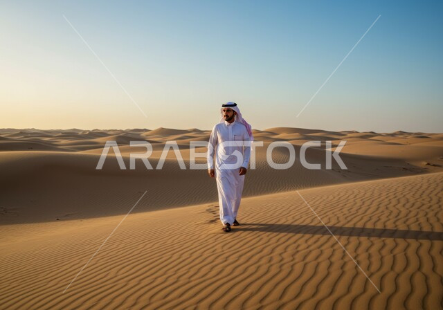 رحلة ونشاط ترفيهي على المال الذهبية الناعمة، الاستمتاع بالمناظر الطبيعية في الصحاري في النهار، رجل عربي خليجي سعودي يرتدي الشماغ والثوب التقليدي يقوم بالتجول في المناطق الصحراوية، التلال والكثبان الرملية في الصحراء، خلفية الطبيعة