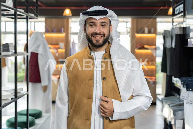 التبضع وأخذ الحاجات اللازمة، التجول داخل أحد المولات التجارية الفاخرة ، رجل عربى خليجي اماراتي مبتسم يرتدي الكندورة البيضاء يقف مبتسم داخل محل ملابس ، شراء واقتناء المستلزمات من المولات، عرض الأزياء والموديلات الحديثة