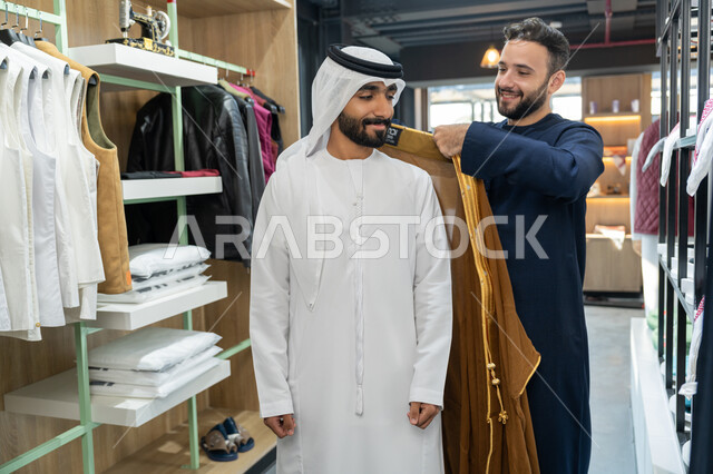 اتقان صنع الملابس، أخذ القياسات المناسبة ، اختراع وابتكار موديلات جديدة وعصرية، حرف ومهن يدوية،شاب خليجي اماراتي يرتدي الكندورة يقوم بقياس الملابس ، فن الخياطة وتصميم ازياء