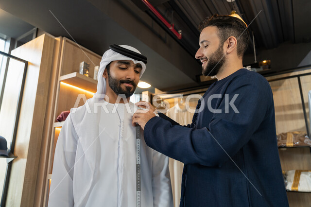 استعمال أدوات ومعدات الخياطة، حرف ومهن يدوية، ممارسة مهنة الخياطة، خياط عربي خليجي اماراتي يرتدي الكندورة الزرقاء يستخدم شريط القياس لتحديد المقاسات، متعه التسوق في المول،  اختيار اجود انواع الأقنشة لتفصيل الثوب
