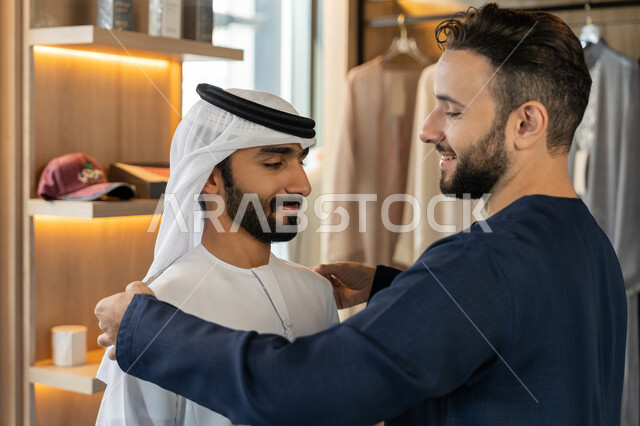 شراء الملابس والاكسسوارات الجديدة، استعمال أدوات ومعدات الخياطة، حرف ومهن يدوية، صورة مقربه ليد خياط عربي خليجي اماراتي يرتدي الكندورة الزرقاء يقوم باخذ مقاس الزبون، اختيار أجود أنواع الأقمشة لصناعة الأثواب،  الجمعة البيضاء
