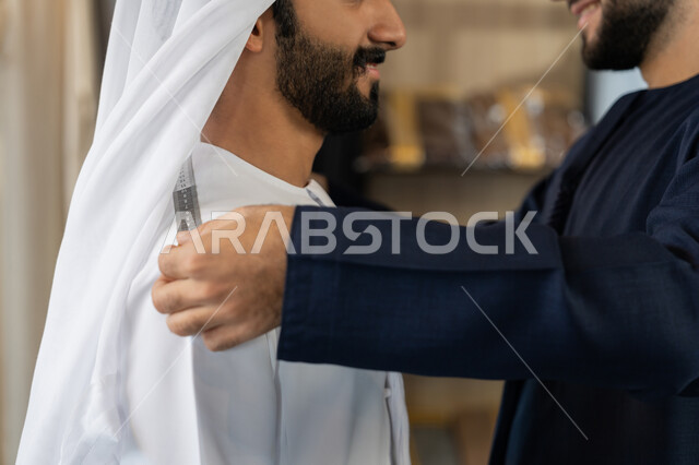 حرف ومهن يدوية، إتقان صنع الملابس ، ممارسة مهنة الخياطة، صورة مقربه ليد خياط عربي خليجي اماراتي يرتدي الكندورة الزرقاء يقوم باخذ مقاس الزبون، اختيار أجود أنواع الأقمشة لصناعة الأثواب، متعه التسوق في المول