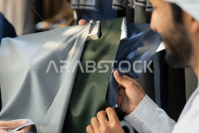 التسوق من الماركات العالميه، تعابير وايماءات السرور والسعادة، عرض الأزياء والموديلات الحديثة،  صورة مقربة لرجل عربي خليجي اماراتي يرتدي الثوب التقليدي يقوم بشراء الملابس، متعه التسوق و شراء الملابس الجديده، قضاء وقت ممتع في التسوق