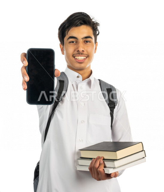 A portrait of a Saudi Arabian Gulf university student holding university books in his hand and displaying a mobile phone screen, university platforms for distance education, communication and chatting with colleagues, follow-up and remote planning, the de