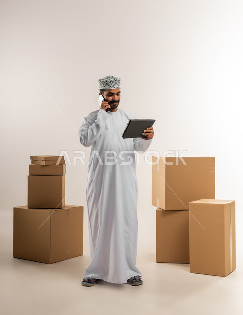 الرد على الاتصالات والاستفسارات من الزبائن, بورتريه لرجل عربي خليجي عماني يرتدي الكمة والدشداشة يعمل في خدمة العملاء في شركة شحن وتوصيل البضائع, توثيق الطلبات من التابلت, تاكيد الحجوزات ادارة عملية خدمات التوصيل السريع, الجسم بالطول الكامل، خلفية بيضاء