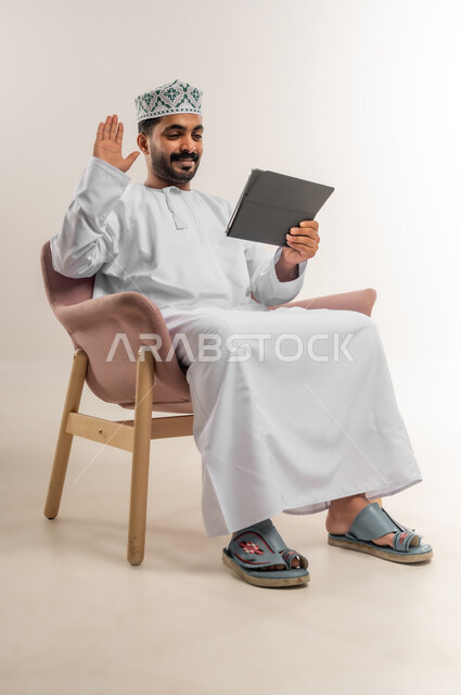 الدردشة مع الأهل والأصدقاء، استعمال التكنولوجيا والتقنيات الحديثة، بورتريه لرجل عربي خليجي عماني يرتدي الدشداشة والكمة يحمل بيده جهاز التابلت، تصفح مواقع التواصل الاجتماعي، استخدام تطبيقات وبرامج الأجهزة اللوحية، خلفية بيضاء