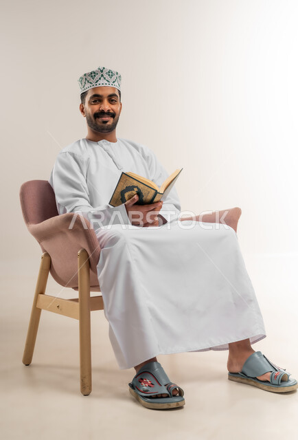تلاوة وقراءة القرآن الكريم وتدبر معانيه، بورتريه لرجل عربي خليجي عماني يرتدي الدشداشة والكمة يحمل بيده المصحف الشريف، الإكثار من ذكر الله تعالى، الشعور بالخشوع والطمأنينة، خلفية بيضاء