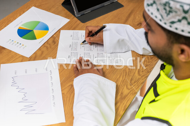 دراسة الرسوم البيانية والاحصاءات، متابعة مخطط الاعمار, العمل في القطاع الهندسي، مفهوم الهندسة والانشاءات المعمارية، بورتريه مقرب لمهندس عربي خليجي عماني يرتدي الدشداشة والكمة وسترة الحماية يمسك بيده التابلت، مهنة ووظيفة للشباب في سلطنة عمان، خلفية بيضاء