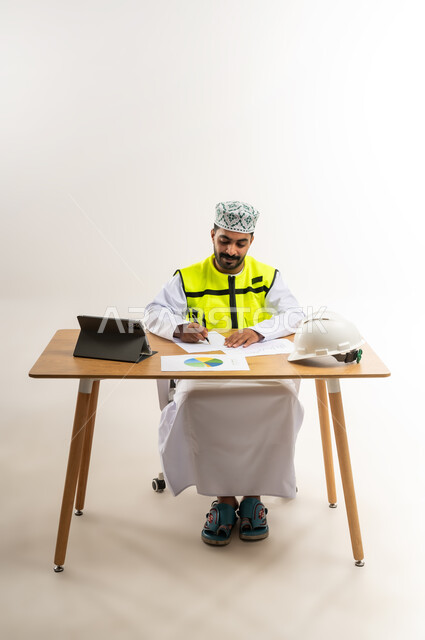 دراسة الرسوم البيانية والاحصاءات، متابعة مخطط الاعمار عبر الجهاز القني, العمل في القطاع الهندسي، مفهوم الهندسة والانشاءات المعمارية، بورتريه لمهندس عربي خليجي عماني يرتدي الدشداشة والكمة وسترة الحماية يمسك بيده التابلت، مهنة ووظيفة للشباب في سلطنة عمان، خلفية بيضاء