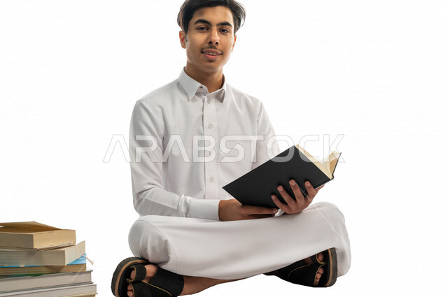 بورتريه لطالب جامعي عربي خليجي سعودي يجلس بين مجموعة من الكتب الجامعية ،الاستمتاع بقراءة الكتاب الجامعي ،المذاكرة للاختبارات الجامعية ، مراجعة الدروس اليومية ، التعليم الجامعي في المملكة العربية السعودية