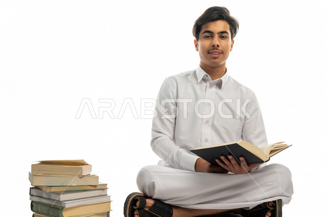 بورتريه لطالب جامعي عربي خليجي سعودي يجلس بين مجموعة من الكتب الجامعية ،الاستمتاع بقراءة الكتاب الجامعي ،المذاكرة للاختبارات الجامعية ، مراجعة الدروس اليومية ، التعليم الجامعي في المملكة العربية السعودية