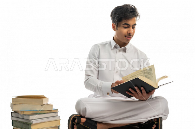بورتريه لطالب جامعي عربي خليجي سعودي يجلس بين مجموعة من الكتب الجامعية ،الاستمتاع بقراءة الكتاب الجامعي ،المذاكرة للاختبارات الجامعية ، مراجعة الدروس اليومية ، التعليم الجامعي في المملكة العربية السعودية