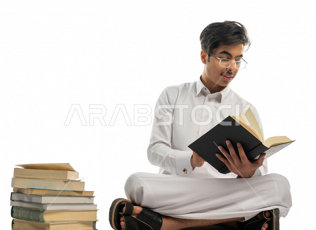 بورتريه لطالب جامعي عربي خليجي سعودي يجلس بين مجموعة من الكتب الجامعية ،الاستمتاع بقراءة الكتاب الجامعي ،المذاكرة للاختبارات الجامعية ، مراجعة الدروس اليومية ، التعليم الجامعي في المملكة العربية السعودية