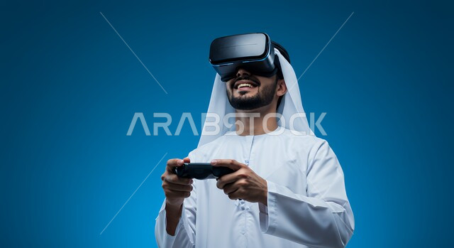 قضاء وقت فراغ ممتع، جهاز تكنولوجي وتقنية حديثة، دمج المتعة والتسلية مع العالم الافتراضي، بورتريه مقرب لشاب عربي خليجي اماراتي يرتدي الكندورة والغترة ونظارة الفي آر يمسك بيده عصا التحكم يقوم باللعب في ألعاب الفيديو الترفيهية، خلفية ز رقاء
