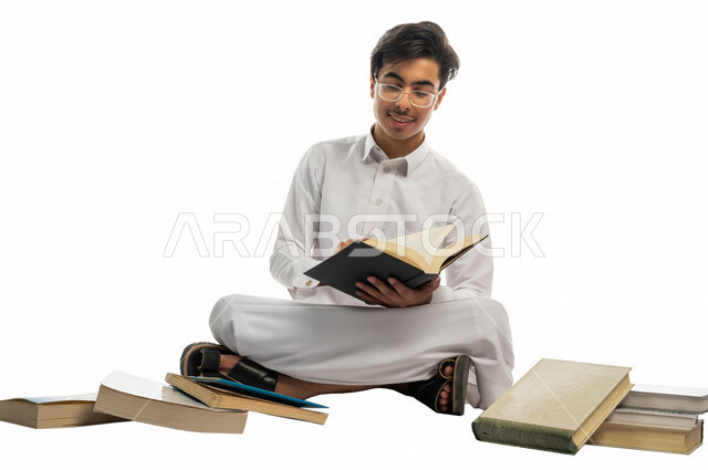 Portrait of a Saudi Arabian Gulf university student sitting among a group of university books, enjoying reading the university book, studying for university exams, reviewing daily lessons, university education in the Kingdom of Saudi Arabia