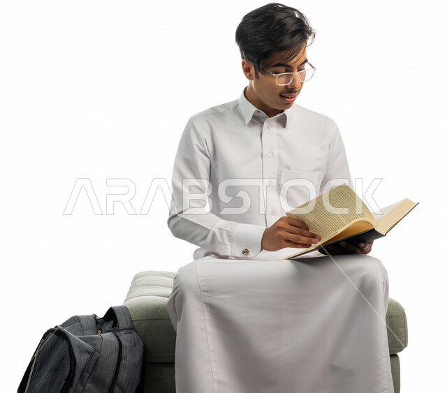 بورتريه لطالب جامعي عربي خليجي سعودي يجلس وبجانبه حقيبة الكتب ، مستمتع بقراءة الكتاب الجامعي ،المذاكرة للاختبارات الجامعية ، مراجعة الدروس اليومية ، التعليم الجامعي في المملكة العربية السعودية