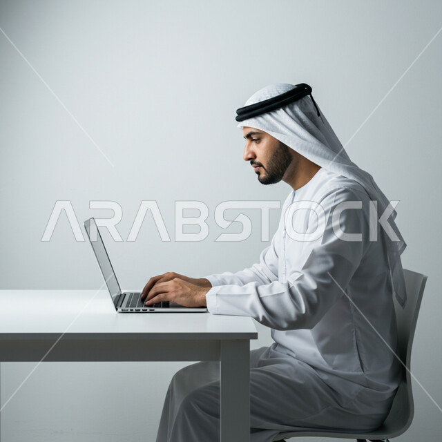  العمل في مكاتب وشركات الامارات العربية المتحدة، أداء المهام والاعمال المكتبية داخل مقر الشركة، بورتريه من الجانب لرجل عربي خليجي اماراتي يرتدي الكندورة والغترة يجلس أمام مكتبه يقوم بالعمل على الحاسب المحمول، دمج التقنية والتكنولوجيا في الحياة العملية، خلفية بيضاء