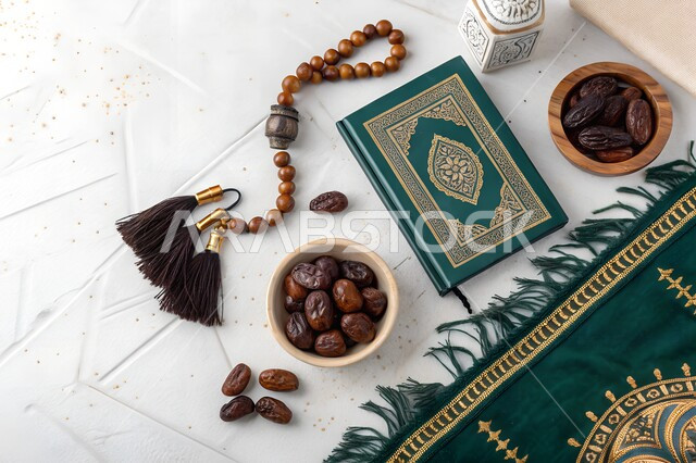 الجو الديني الروحاني في شهر رمضان المبارك, الاجتهاد في الدعاء وطلب المغفرة في الشهر الفضيل، العبادة والتقرب إلى الله، التعبد بتلاوة القران وحفظ وتفسير كلامه، افطار الصائم بحباب التمر الطازجة، صورة علوية لسجادة صلاة بجانب المصحف الشريف وسبحة وطبق من الرطب