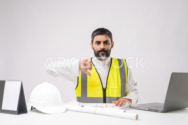 Failure in engineering and construction project management, integration of technology in engineering, working in the engineering sector, youth career and job, portrait of a Saudi Arabian Gulf engineer wearing a protective vest working on a laptop with his thumb down, white background