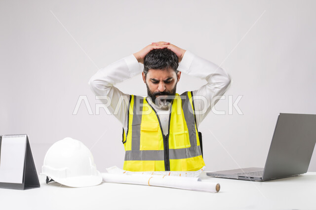 ايماءات الاجهاد والتعب والتفكير، دمج التقنية والتكنولوجيا في مجال الهندسة، العمل في القطاع الهندسي، مفهوم ادارة المشاريع الهندسية والانشاءات، مهنة ووظيفة شبابية، بورتريه لمهندس عربي خليجي سعودي يرتدي الثوب التقليدي والسترة يعمل على الحاسوب المحمول، خلفية بيضاء