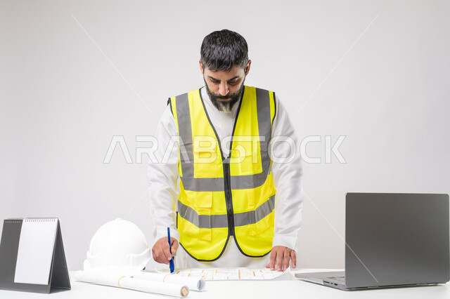Integrating technology and technology in the field of engineering, working in the engineering sector in the Kingdom of Saudi Arabia, the concept of engineering and construction project management, a youth profession and job, a portrait of a Saudi Arabian Gulf engineer wearing a traditional thobe and jacket working on a laptop, white background