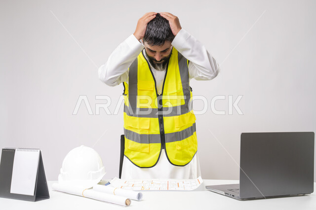 Failure in engineering and construction project management, integration of technology in the field of engineering, work in the engineering sector, youth profession and job, portrait of a Saudi Arabian Gulf engineer wearing a protective vest working on a laptop with his hands on his head with an expression of despair, white background