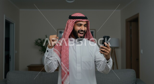 Achieving goals and accomplishments, expressions of victory and triumph, a close-up of a Saudi Arabian Gulf man wearing a traditional shemagh and thobe holding a mobile phone, raising his fist with gestures of enthusiasm and pleasure, seeing happy and joyful news