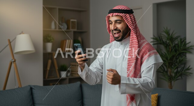 رؤية الاخبار المفرحة والسعيدة، تحقيق الاهداف والانجاز، تعابير النصر والفوز، صورة مقربة لرجل عربي خليجي سعودي يرتدي الشماغ والثوب التقليدي يمسك بيده الهاتف المحمول يرفع قبضة يده للاعلى بايماءات الحماس والسرور