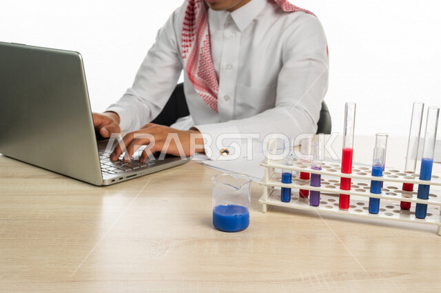Portrait of a Saudi Arabian Gulf university student sitting in a chemistry lab, using a laptop computer to learn molecular structures and interactions, using test tubes to conduct experiments in the laboratory, chemical reactions, research and development