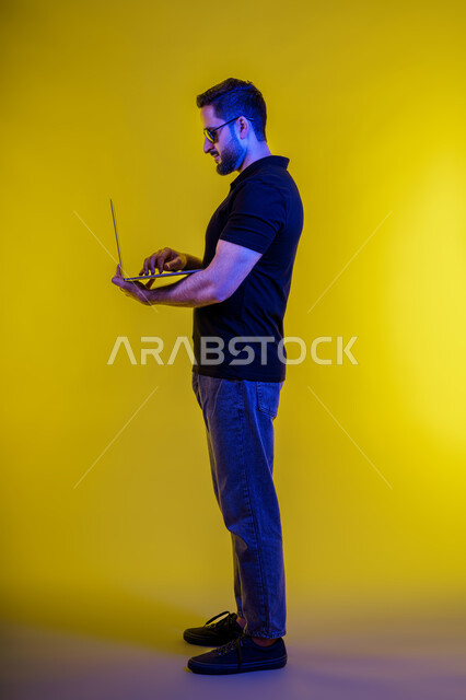 Making a video call using a laptop, portrait of a young Emirati Gulf man in casual clothes, a Saudi Arabian man browsing the internet, using modern technical devices, remote work, electronic marketing, professions and jobs, holding a business meeting via laptop, yellow background