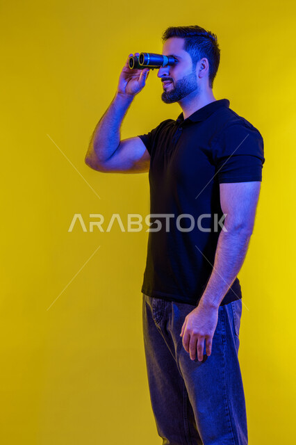 Saudi man looking through binoculars, full-length portrait of a young Arab Gulf Emirati man wearing casual clothes, yellow background, seeing distant objects using a telescope, using binoculars and the love of exploration and adventure, planning for future goals and ambitions