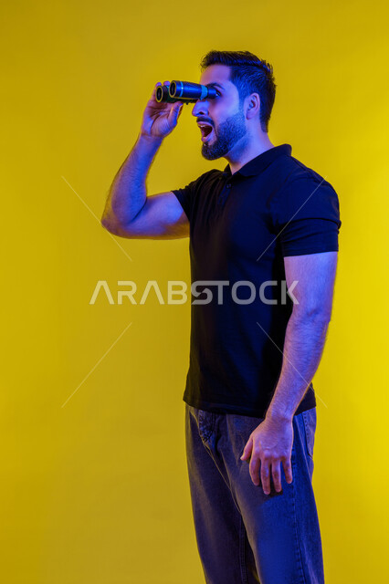 Signs of surprise on a Saudi man looking through binoculars, full-length portrait of a young Arab Gulf Emirati man wearing casual clothes, yellow background, seeing distant objects using a telescope, using binoculars and the love of exploration and adventure, planning for future goals and ambitions
