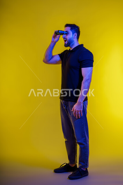 Gestures of surprise on a Saudi man looking through binoculars, full-length portrait of a young Arab Gulf Emirati man wearing casual clothes, yellow background, seeing distant objects using a telescope, using binoculars and the love of exploration and adventure, planning for future goals and ambitions