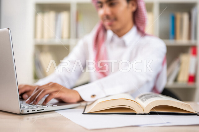 طالب جامعي عربي خليجي سعودي يرتدي الزي الخليجي التقليدي ،يقضي وقت ممتع في مكتبة الجامعة ،يستخدم الحاسوب المحمول داخل المكتبة ، استخدام التكنولوجيا في التعلم ،استعارة كتاب مناسب ، اثراء التعليم الجامعي ، البحث العلمي ، مفهوم التعليم والتعلم