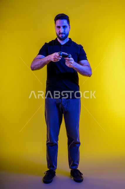 Entertainment video games, fun and entertainment on PlayStation, a young Saudi Arabian Gulf man holding a joystick, a portrait of an Emirati young man wearing casual clothes and showing happy gestures, having a good time, yellow background