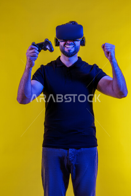 PlayStation entertainment technologies and games, fun and entertainment with video games, a young Saudi Arabian Gulf man holding a joystick and wearing virtual reality glasses, a portrait of an Emirati young man wearing casual clothes and enjoying VR technology, having a good time, a yellow hidden camera