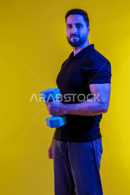 اللياقة الجسدية والقوة البدنية لرجل سعودي ، الاهتمام بالصحة ، رياضة كمال الأجسام، البناء العضلي والثقة، استخدام الأوزان الحديدية الرياضية، بورتريه لشاب عربي خليجي اماراتي يرتدي الزي الكاجوال، أسلوب حياة صحي، خلفية صفراء