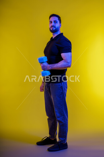 Physical strength of a Saudi man, interest in health and fitness, bodybuilding, muscle building and confidence, using iron weights, full-length portrait of a young Arab Gulf Emirati man wearing casual clothes, healthy lifestyle, yellow background