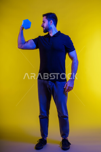Muscle building, strength and confidence, using iron weights, full-length portrait of a young Arab Gulf Emirati man wearing casual clothes, bodybuilding, healthy lifestyle, interest in health and physical fitness, Saudi man practicing muscle strengthening activities, yellow background